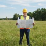 Na tym obrazku widać mężczyznę stojącego na środku rozległej, zielonej łąki pokrytej wysoką trawą